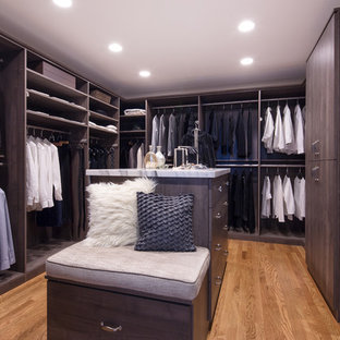Immagine di una grande cabina armadio unisex design con ante lisce, ante grigie e pavimento in legno massello medio