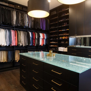Modelo de armario vestidor unisex, moderno, grande, con armarios con paneles lisos, puertas de armario negras, suelo de madera oscura y suelo marrón