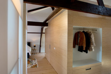 Example of a minimalist gender-neutral light wood floor reach-in closet design in Amsterdam with flat-panel cabinets and light wood cabinets