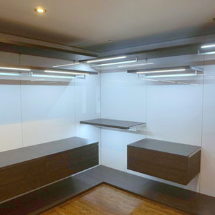 Foto di una grande cabina armadio unisex moderna con ante lisce, ante in legno bruno e pavimento in legno massello medio