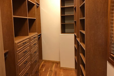 Example of a mid-sized classic gender-neutral medium tone wood floor and brown floor walk-in closet design in Other with raised-panel cabinets and medium tone wood cabinets