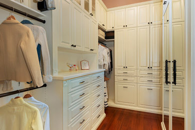 Diseño de armario vestidor de mujer tradicional grande con armarios con paneles con relieve, puertas de armario blancas y suelo de madera en tonos medios