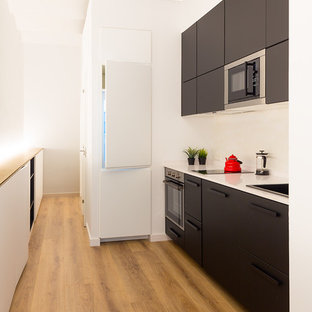 Modelo de cocina lineal, actual, pequeña, abierta, sin isla, con armarios con paneles lisos, puertas de armario negras, salpicadero blanco, encimeras blancas, suelo de madera en tonos medios, suelo marrón, fregadero de un seno y electrodomésticos con paneles