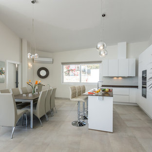 Imagen de cocina comedor en L, actual, con armarios con paneles lisos, puertas de armario blancas, electrodomésticos negros, una isla, suelo gris, fregadero bajoencimera, salpicadero verde, salpicadero de vidrio templado y encimeras negras