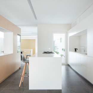 Imagen de cocina comedor de galera, minimalista, con armarios con paneles lisos, puertas de armario blancas, una isla, fregadero bajoencimera, salpicadero blanco, electrodomésticos con paneles, suelo gris y encimeras blancas