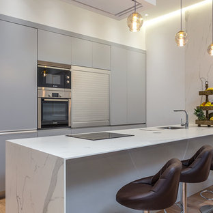 Imagen de cocina lineal, contemporánea, de tamaño medio, con armarios con paneles lisos, puertas de armario grises, encimera de mármol, suelo de madera en tonos medios, península, encimeras blancas, fregadero bajoencimera y electrodomésticos de acero inoxidable