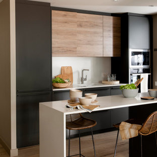 Ejemplo de cocina de galera, contemporánea, con fregadero bajoencimera, armarios con paneles lisos, puertas de armario negras, salpicadero blanco, salpicadero de losas de piedra, electrodomésticos de acero inoxidable, suelo de madera en tonos medios, una isla, suelo marrón y encimeras blancas