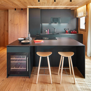 Ejemplo de cocina comedor de galera, minimalista, grande, con fregadero de un seno, armarios con paneles lisos, puertas de armario negras, encimera de piedra caliza, salpicadero negro, salpicadero de piedra caliza, electrodomésticos de acero inoxidable, una isla, encimeras negras, suelo de madera clara y suelo beige