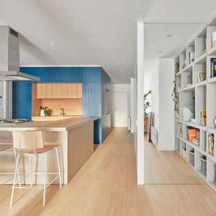 Diseño de cocina en U, contemporánea, abierta, con puertas de armario azules, electrodomésticos blancos, suelo de madera clara, península, suelo marrón, encimeras beige, armarios con puertas mallorquinas, salpicadero beige y salpicadero de vidrio