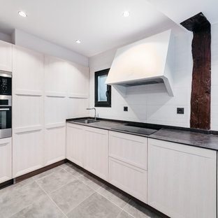 Imagen de cocina en L, actual, sin isla, con fregadero bajoencimera, armarios con rebordes decorativos, puertas de armario de madera clara, salpicadero blanco, electrodomésticos de acero inoxidable, suelo gris y encimeras negras
