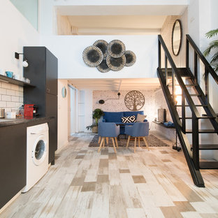 Diseño de cocina de galera, urbana, abierta, sin isla, con fregadero encastrado, armarios con paneles lisos, puertas de armario negras, salpicadero blanco, salpicadero de azulejos tipo metro, electrodomésticos blancos, suelo de madera pintada, suelo beige y encimeras negras