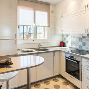 Diseño de cocina en L, clásica renovada, con fregadero bajoencimera, puertas de armario blancas, electrodomésticos de acero inoxidable, suelo de baldosas de cerámica, encimeras grises, armarios con paneles con relieve, salpicadero multicolor y suelo multicolor