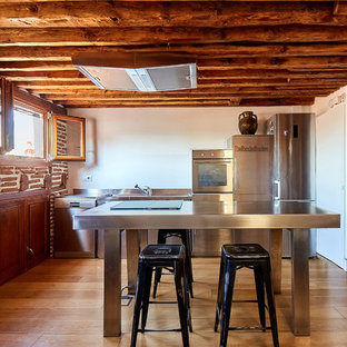 Imagen de cocina comedor lineal, rústica, pequeña, con fregadero de un seno, puertas de armario en acero inoxidable, encimera de acero inoxidable, electrodomésticos de acero inoxidable, suelo de madera en tonos medios, una isla, suelo marrón, armarios con paneles lisos, salpicadero marrón y encimeras grises