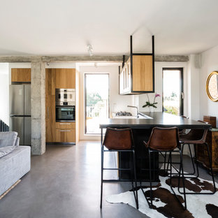 Modelo de cocina contemporánea, abierta, con puertas de armario de madera oscura, suelo de cemento, una isla, encimeras negras, armarios con paneles lisos y suelo gris
