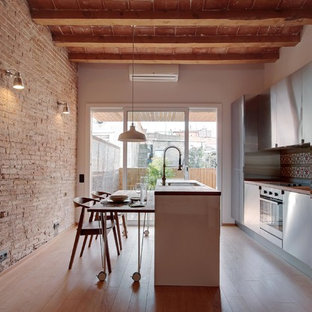Cette image montre une grand cuisine américaine parallèle urbaine avec un placard à porte plane, une façade en inox, une crédence multicolore, une crédence en carreau de céramique, un électroménager en acier inoxydable, un sol en bois clair, un îlot central et un évier posé.