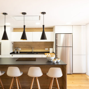Foto de cocina comedor contemporánea con fregadero encastrado, armarios con paneles lisos, puertas de armario blancas, salpicadero marrón, salpicadero de madera, electrodomésticos de acero inoxidable, suelo de madera en tonos medios, una isla, suelo marrón y encimeras negras