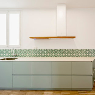 Immagine di una cucina design di medie dimensioni con lavello sottopiano, ante lisce, ante turchesi, paraspruzzi verde, paraspruzzi con piastrelle di cemento, pavimento in legno massello medio, nessuna isola, pavimento multicolore e top bianco
