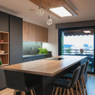 Modern inredning av ett stort brun linjärt brunt kök med öppen planlösning, med en rustik diskho, släta luckor, svarta skåp, träbänkskiva, svart stänkskydd, svarta vitvaror, mellanmörkt trägolv och en köksö
