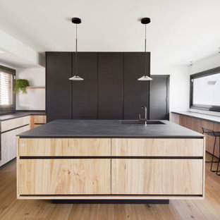 Ejemplo de cocina en U, minimalista, con fregadero bajoencimera, armarios con paneles lisos, puertas de armario de madera clara, suelo de madera clara, una isla, suelo beige y encimeras negras