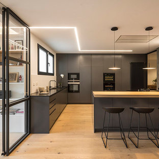 Foto di una grande cucina contemporanea con ante lisce, ante nere, penisola, lavello sottopiano, paraspruzzi bianco, elettrodomestici neri e parquet chiaro