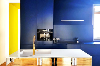 Imagen de cocina lineal contemporánea de tamaño medio abierta con fregadero sobremueble, armarios estilo shaker, puertas de armario azules, encimera de cuarzo compacto, salpicadero azul, suelo de madera en tonos medios, una isla y encimeras blancas