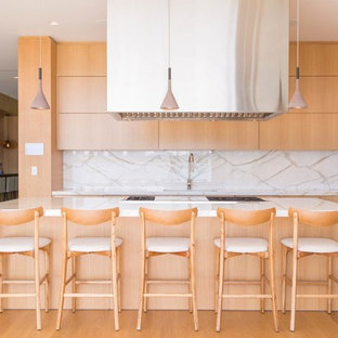 Ejemplo de cocina lineal, contemporánea, grande, con fregadero bajoencimera, armarios con paneles lisos, puertas de armario de madera clara, encimera de cuarzo compacto, salpicadero blanco, suelo de madera en tonos medios, una isla, encimeras blancas y suelo marrón