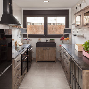 Imagen de cocina en U, tradicional renovada, sin isla, con fregadero de doble seno, armarios con paneles lisos, puertas de armario de madera oscura, salpicadero blanco, electrodomésticos negros, suelo gris y encimeras negras