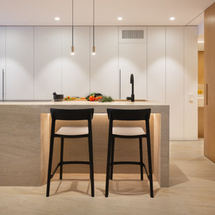 Foto de cocina en L, actual, extra grande, abierta, con armarios con paneles lisos, puertas de armario blancas, encimera de piedra caliza, una isla, encimeras marrones, fregadero integrado, electrodomésticos con paneles y suelo beige