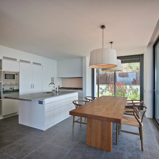 Modelo de cocina comedor en L, moderna, con fregadero bajoencimera, armarios con paneles lisos, puertas de armario blancas, electrodomésticos de acero inoxidable, una isla, suelo gris y encimeras grises