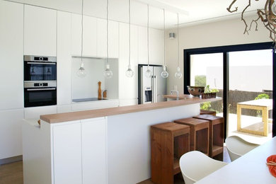 Moderne Wohnküche mit Küchengeräten aus Edelstahl, braunem Holzboden, weißer Arbeitsplatte, Kücheninsel, flächenbündigen Schrankfronten, weißen Schränken und Küchenrückwand in Weiß in Sonstige