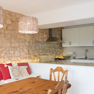 Ejemplo de cocina comedor en U, mediterránea, con fregadero encastrado, armarios con paneles lisos, puertas de armario blancas, península, salpicadero beige, salpicadero de vidrio templado y encimeras beige