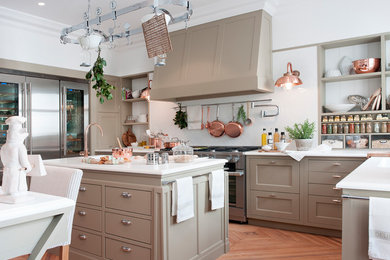Klassisk inredning av ett kök och matrum, med en integrerad diskho, beige skåp, bänkskiva i kvarts, vitt stänkskydd, stänkskydd i keramik, rostfria vitvaror, ljust trägolv, en köksö och brunt golv