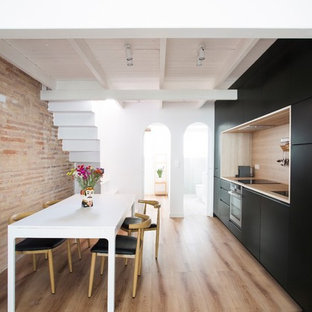Ejemplo de cocina comedor lineal, actual, con armarios con paneles lisos, puertas de armario negras, encimera de madera, salpicadero de vidrio y suelo de madera clara