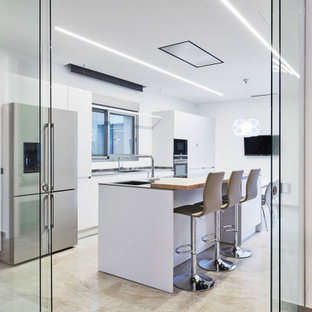 Imagen de cocina de galera, contemporánea, cerrada, con armarios con paneles lisos, puertas de armario blancas, electrodomésticos de acero inoxidable, una isla, suelo beige y encimeras grises