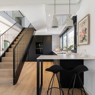 Diseño de cocinas en L contemporánea, de tamaño medio, abierta, con fregadero bajoencimera, armarios con paneles lisos, puertas de armario negras, salpicadero de vidrio, electrodomésticos con paneles, península, suelo beige y encimeras grises