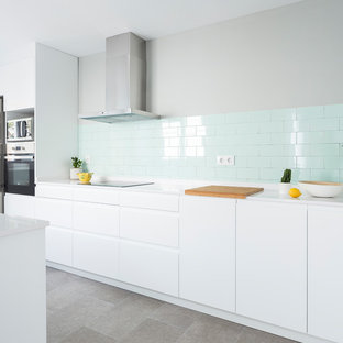 Imagen de cocina lineal, contemporánea, con armarios con paneles lisos, puertas de armario blancas, salpicadero gris, salpicadero de azulejos tipo metro, electrodomésticos de acero inoxidable, una isla, suelo gris y encimeras blancas