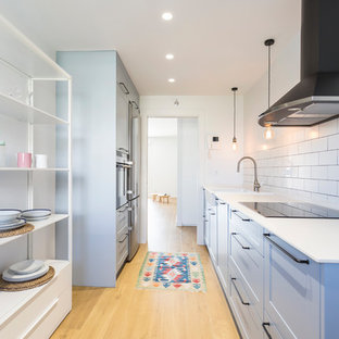 Diseño de cocina de galera, escandinava, cerrada, sin isla, con fregadero sobremueble, armarios estilo shaker, puertas de armario azules, salpicadero blanco, salpicadero de azulejos tipo metro, suelo de madera clara y encimeras blancas