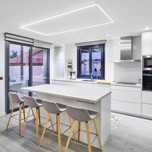 Diseño de cocina en L, actual, con fregadero bajoencimera, armarios con paneles lisos, puertas de armario blancas, electrodomésticos de acero inoxidable, una isla, suelo gris y encimeras blancas
