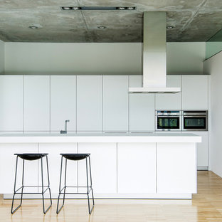 Ejemplo de cocina minimalista con armarios con paneles lisos, puertas de armario blancas, electrodomésticos de acero inoxidable, una isla, suelo beige y encimeras blancas