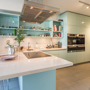 Foto de cocina en L, moderna, extra grande, con fregadero bajoencimera, armarios con paneles lisos, puertas de armario azules, salpicadero blanco, electrodomésticos de acero inoxidable, península, suelo gris y encimeras blancas