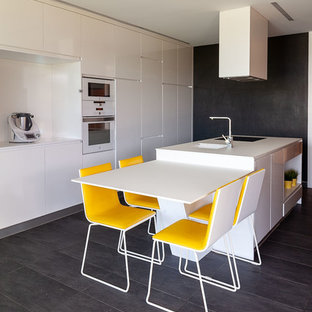 Ejemplo de cocina comedor de galera, actual, con fregadero bajoencimera, armarios con paneles lisos, puertas de armario blancas, salpicadero blanco, electrodomésticos blancos, una isla, suelo gris y encimeras blancas