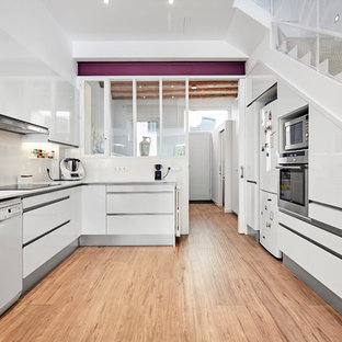 Diseño de cocina en U, contemporánea, cerrada, sin isla, con armarios con paneles lisos, puertas de armario blancas, salpicadero beige, electrodomésticos blancos, suelo de madera en tonos medios, suelo beige y encimeras blancas