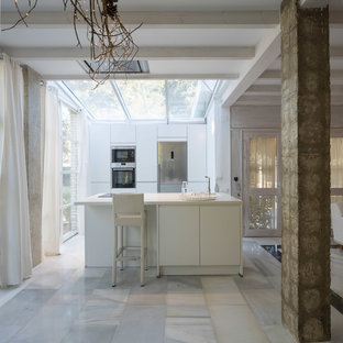 Imagen de cocina lineal, actual, con armarios con paneles lisos, puertas de armario blancas, electrodomésticos de acero inoxidable, suelo de mármol, una isla, suelo blanco, encimeras blancas y fregadero bajoencimera