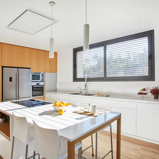 Foto de cocina minimalista con armarios con paneles lisos, puertas de armario blancas, encimera de cuarzo compacto, salpicadero blanco, electrodomésticos de acero inoxidable, suelo de madera en tonos medios, una isla y encimeras blancas