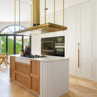 Diseño de cocina comedor de galera, contemporánea, grande, con puertas de armario blancas, encimera de mármol, electrodomésticos negros, suelo de madera clara, una isla, encimeras blancas, armarios con paneles empotrados y suelo beige