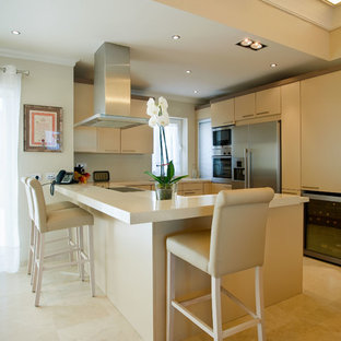 Ejemplo de cocina en U, mediterránea, con armarios con paneles lisos, puertas de armario beige, salpicadero beige, electrodomésticos de acero inoxidable, península, suelo beige y encimeras beige