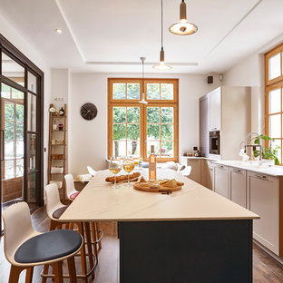 Réalisation d'une cuisine méditerranéenne fermée avec un placard à porte shaker, des portes de placard grises, une crédence en fenêtre, un électroménager de couleur, un sol en bois foncé, un îlot central et un plan de travail blanc.