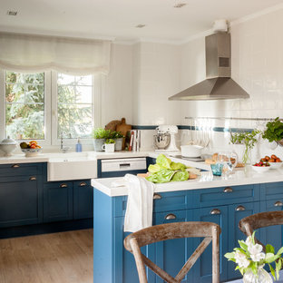 Diseño de cocina comedor en U, clásica renovada, con fregadero sobremueble, armarios estilo shaker, puertas de armario azules, salpicadero blanco, suelo de madera clara, península, suelo marrón y encimeras blancas