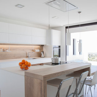 Imagen de cocina costera con fregadero bajoencimera, armarios con paneles lisos, puertas de armario blancas, salpicadero beige, salpicadero de madera, electrodomésticos negros, suelo de madera clara, una isla, suelo beige y encimeras blancas
