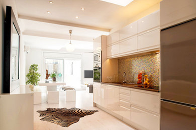 This is an example of a medium sized contemporary single-wall open plan kitchen in Barcelona with flat-panel cabinets, white cabinets, glass tiled splashback, stainless steel appliances and light hardwood flooring.